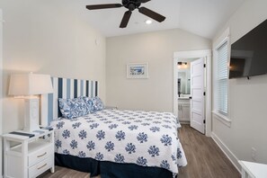 A bedroom with a bed, nightstand, lamp, ceiling fan, and a door leading to a bathroom. - The Lighthouse -Steps to Beach!  Luxury Amenities! (Corolla)