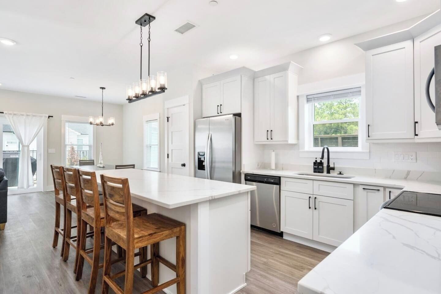 Una cocina moderna con armarios blancos, una isla central con taburetes de bar, electrodomésticos de acero inoxidable y una lámpara colgante.