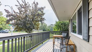 Une terrasse en bois avec une table et des chaises, une rambarde et une vue sur un arbre et la rue.
