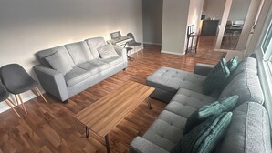 Un salon moderne avec un canapé gris, un pouf assorti, une table basse en bois et un clavier posé sur une petite table.