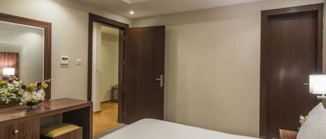 A hotel room with a bed, a desk, a mirror, and a door leading to a bathroom.