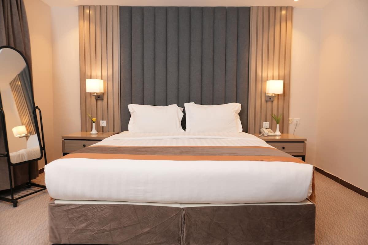 Quarto de hotel com uma cama grande, duas mesas de cabeceira, uma luminária e um espelho.