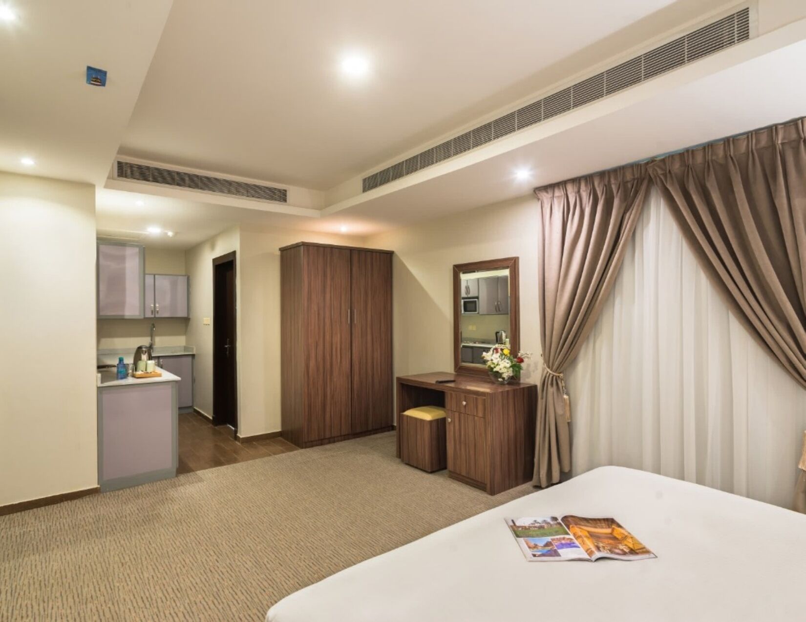 A hotel room with a bed, a desk, a mirror, and a kitchenette.