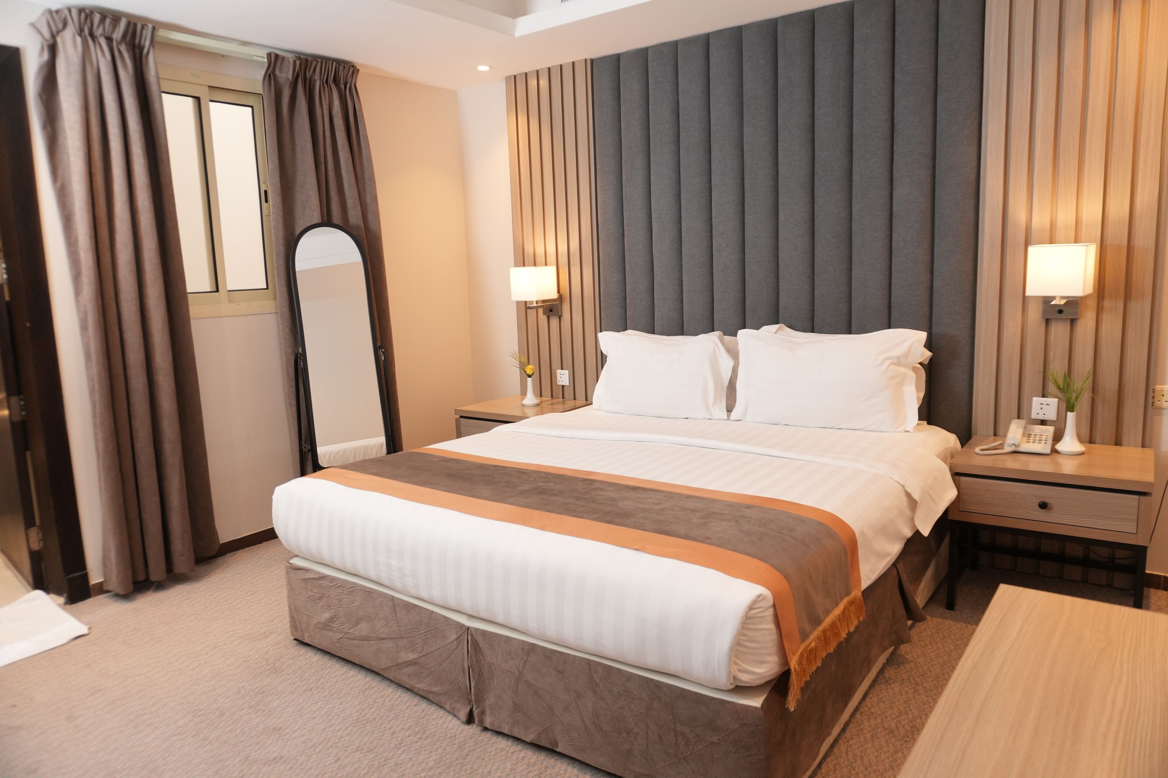 Una habitación de hotel con una cama grande, dos mesitas de noche, un espejo y un buró con una lámpara.