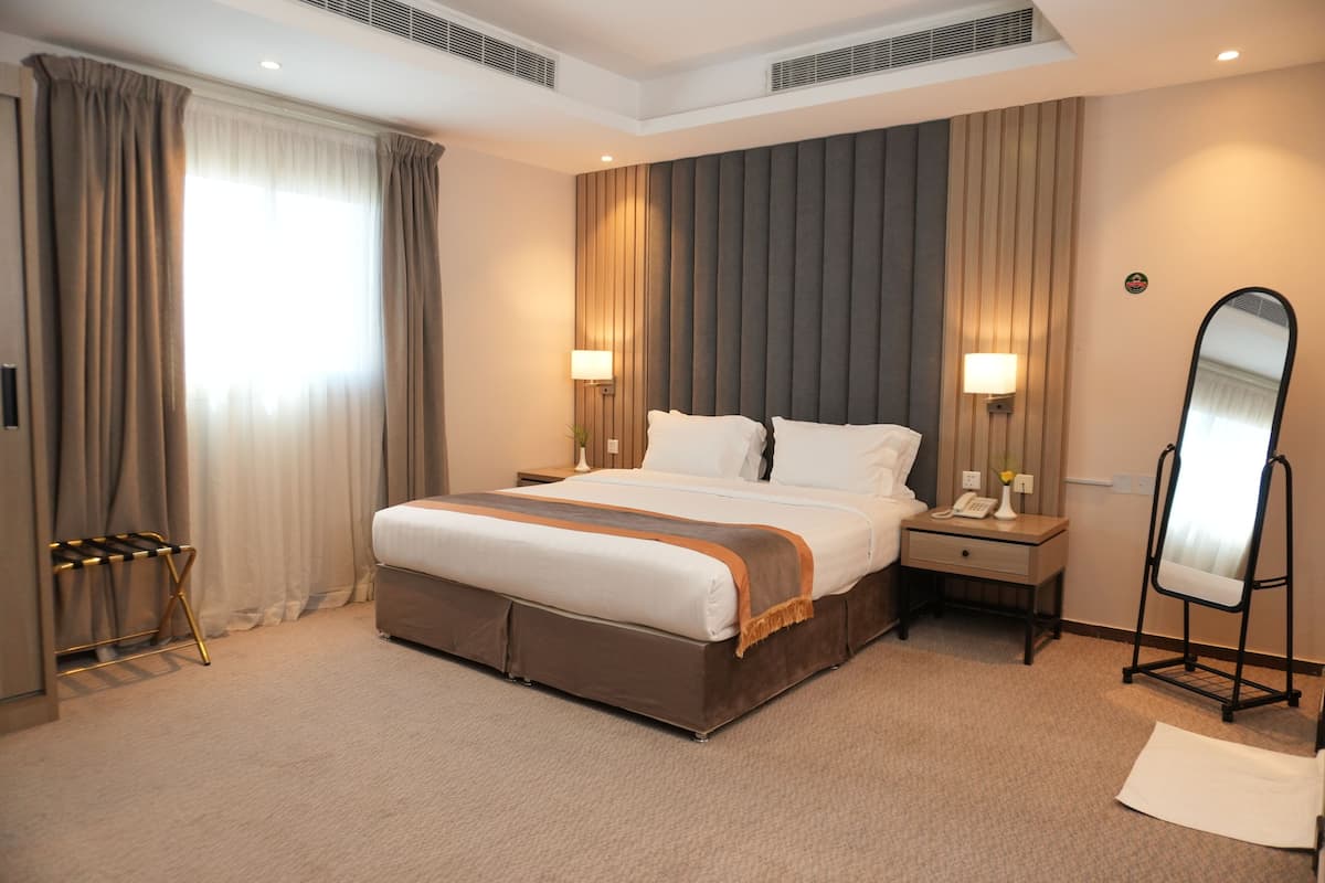 Quarto de hotel com uma cama grande, duas mesas de cabeceira, um espelho e uma janela com cortinas.