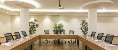 A conference room with a long wooden table, black chairs, and potted plants.