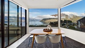 Un espace repas comprenant une table et des chaises, de grandes fenêtres offrant une vue sur les montagnes et un lac, et un aménagement intérieur moderne.