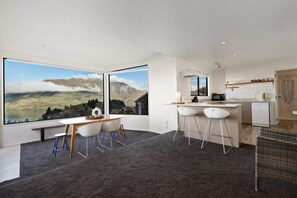 A modern kitchen with large windows, a dining area with a bench, and a view of mountains.