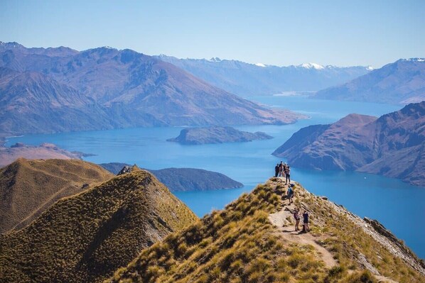 A mountainous landscape with a clear view of a lake and a group of people standing on a ridge. - Wanaka Grandview Lodge (Wānaka)
