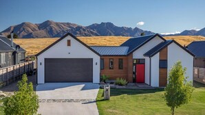 Ett modernt hus i två våningar med ett garage, en röd dörr och utsikt över bergen.