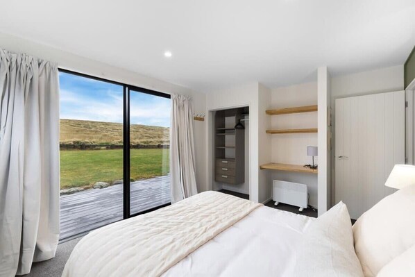 A bedroom with a large bed, a wardrobe, a desk, and a view of a grassy field through a sliding door. - Wanaka Grandview Lodge (Wānaka)
