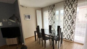 A dining area with a glass table and chairs, a TV on a stand, and a patterned curtain. - Appartement Cosy (Clermont-Ferrand)