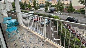A balcony with a tiled floor, a metal railing, and a view of a street with parked cars and buildings in the background. - Appartement Cosy (Clermont-Ferrand)