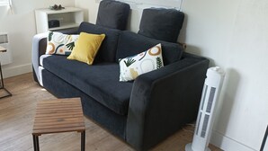 Una sala de estar moderna con un sofá gris oscuro, dos mesitas de madera y un radiador blanco.