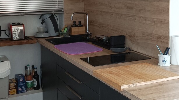Una cocina moderna con encimera de madera, armarios negros y pileta de acero inoxidable.