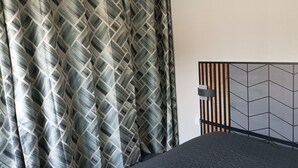 Una habitación con una cama, una cortina de estampado geométrico y un separador con diseño de listones de madera.