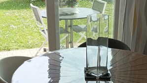 Una mesa con cubierta de vidrio, sillas, vistas a un jardín y una puerta que da al exterior.