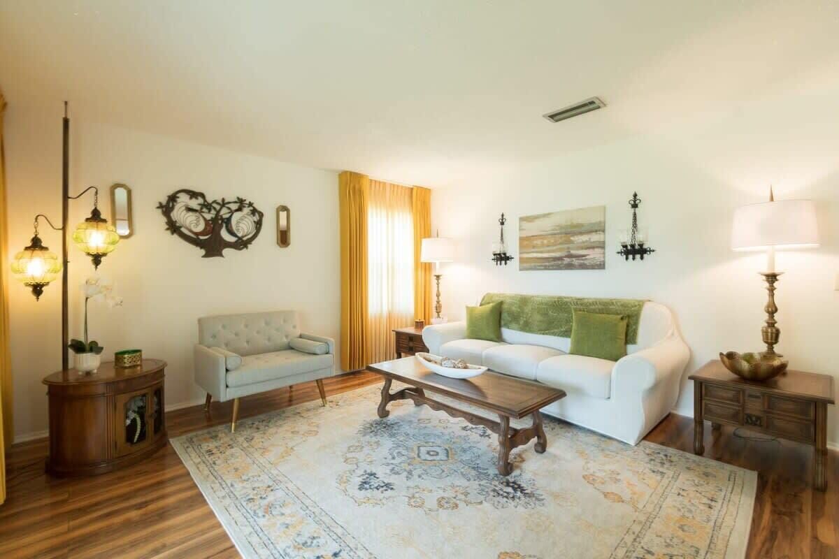 A living room with a white sofa, a wooden coffee table, a patterned rug, and wall-mounted lamps.