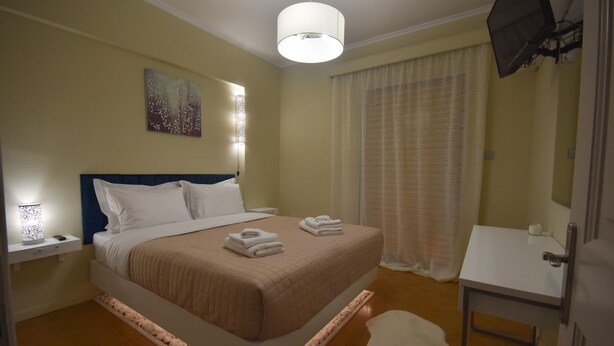 A neatly arranged hotel room with a bed, bedside table, and a small desk with a chair. - K&C Rooms-Apartments (Markopoulo Mesogaias)