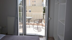 A hotel room with a bed, a balcony with a table and chairs, and a wardrobe. - K&C Rooms-Apartments (Markopoulo Mesogaias)