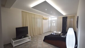 A modern living room with a flat-screen TV on a white stand, a sofa, a coffee table, and a floor lamp. - K&C Rooms-Apartments (Markopoulo Mesogaias)