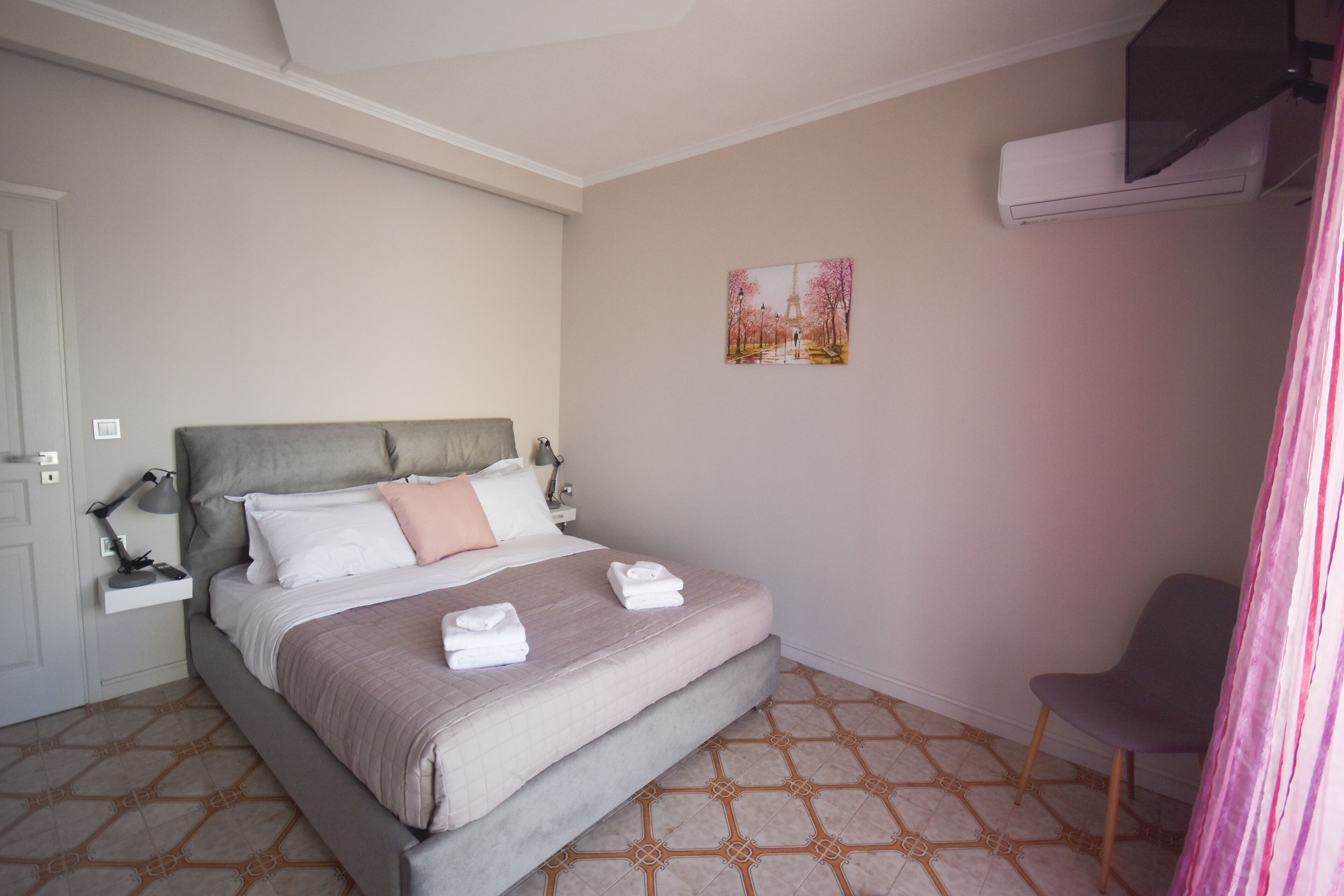 A neatly arranged bedroom with a bed, bedside tables, a chair, and a wall-mounted air conditioner.