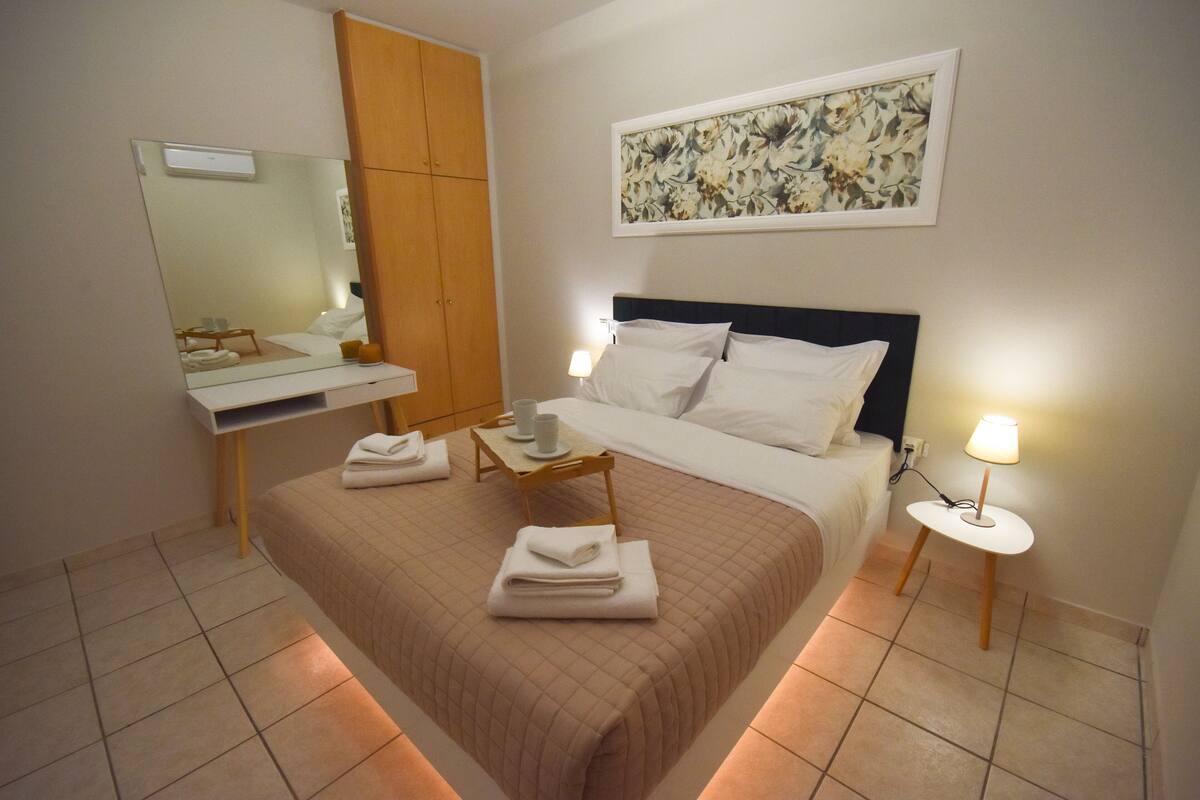 A hotel room with a bed, bedside tables, a mirror, a painting, and a tiled floor.