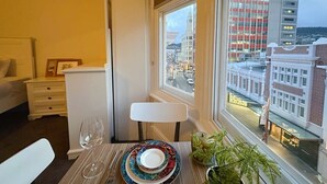 A hotel room with a dining area, a view of the cityscape, a bed, and a nightstand with a lamp. - Central Collins Residence at Inner City (Hobart)