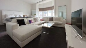 A modern living room with a sectional sofa, a flat-screen TV, and a large window providing natural light. - Central Collins Residence at Inner City (Hobart)