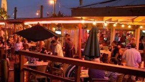 An outdoor dining area with tables and umbrellas, surrounded by a wooden deck and a railing. - Island Breeze Walk to Beach 3/2 Sleeps 10 Okaloosa Island Fort Walton Beach (Fort Walton Beach)