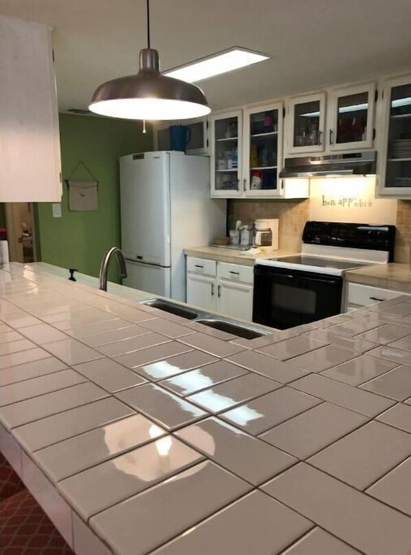 A kitchen with white cabinets, a stainless steel refrigerator, a black stove, and a pendant light.