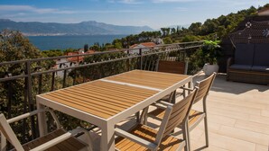 Eine Terrasse mit Tisch und Stühlen mit Blick auf eine malerische Seen- und Berglandschaft.