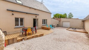 Een huis met een patio, voorzien van een houten terras, een tafel met stoelen en een grindpad.