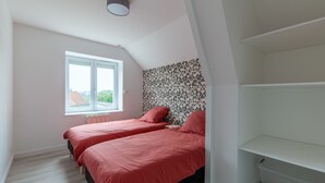 Een slaapkamer met twee bedden, een raam, een radiator en een witte plank.