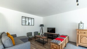Een moderne woonkamer met een grijze bank, een klein tafeltje en een televisie.