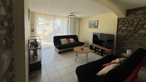 A living room with a sofa, a coffee table, a TV, and a stone wall. - Une Maison à la Mer - Proche de la marina (Saint-Cyprien)