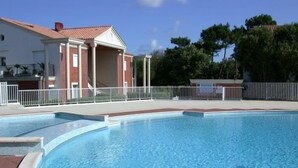 A swimming pool with a clear blue water surface, surrounded by a white fence and a building with a red roof. - L'Hollywood Zen - One Bedroom Apartment, Sleeps 4 (Saint-Jean-de-Monts)