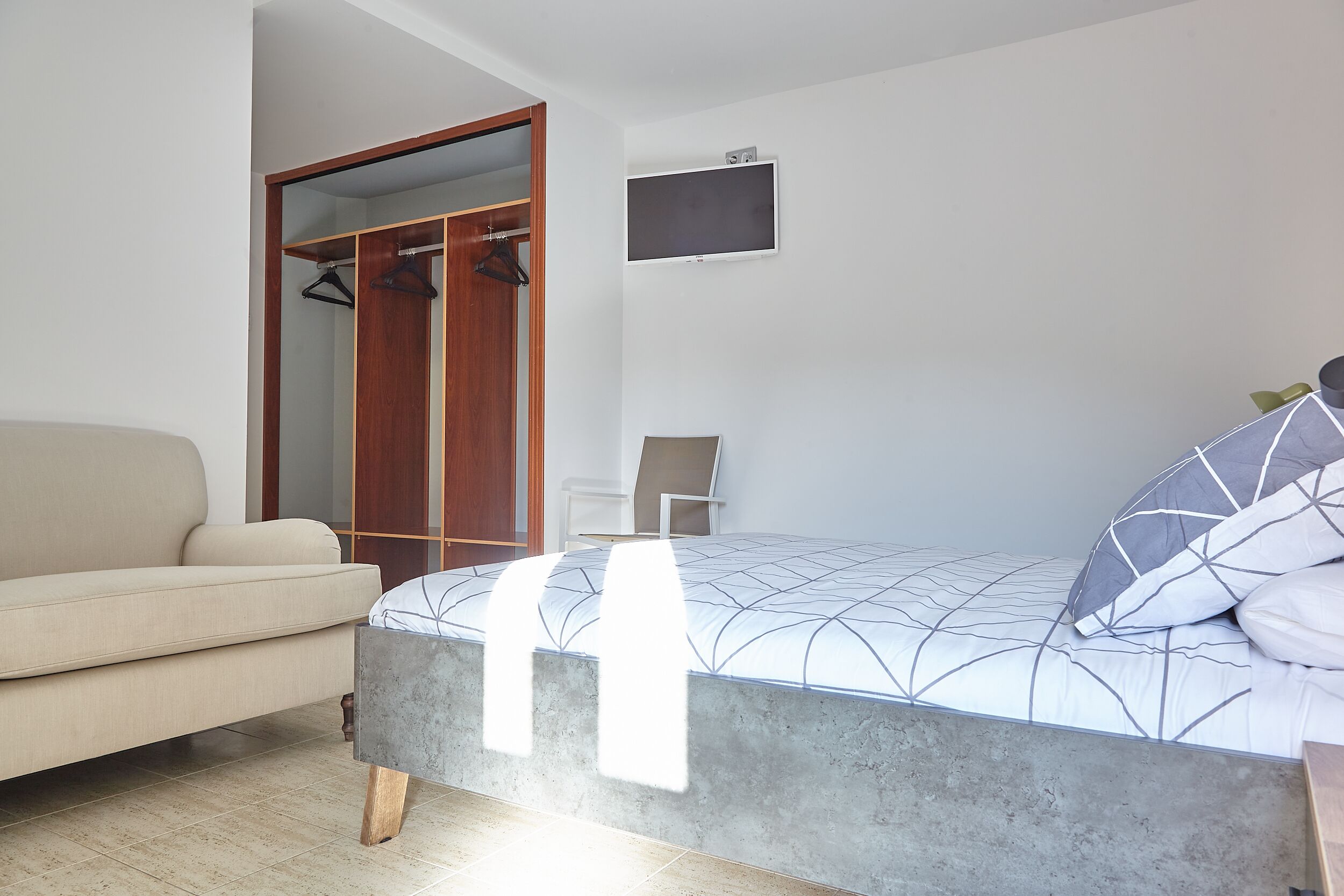 A bedroom with a bed, a sofa, a wardrobe, and a television.