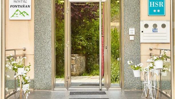 La entrada de un hotel con un toldo de cristal, un cartel que indica que es un hotel y una rampa accesible para sillas de ruedas.