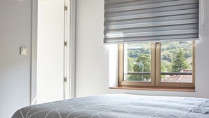 Un dormitorio con cama, ventana con persianas y vista a la vegetación exterior.