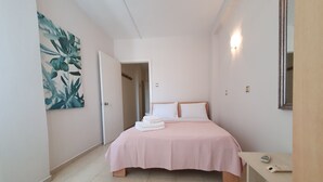 Een slaapkamer met een bed, nachtkastje, spiegel, deur en een plant aan de muur.