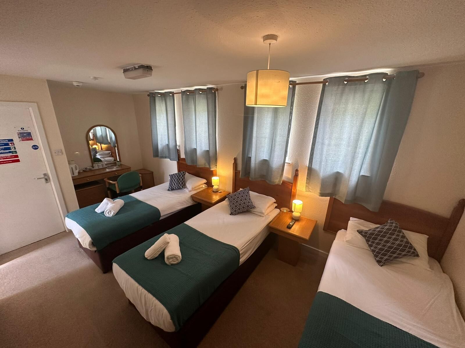 A hotel room with two single beds, a desk with a chair, a mirror, and a window with curtains.