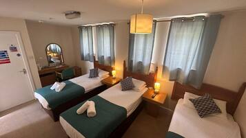 A hotel room with two single beds, a desk with a chair, a mirror, and a window with curtains.