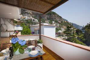 A balcony with a table set for dining, overlooking a hillside town with buildings and greenery.