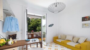 Een lichte woonkamer met een gele bank, een eettafel met stoelen en een keukenhoek.
