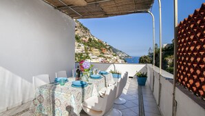 A terrace with a table set for dining, overlooking a coastal town. - Estate4home - Casa Gegé (Positano)