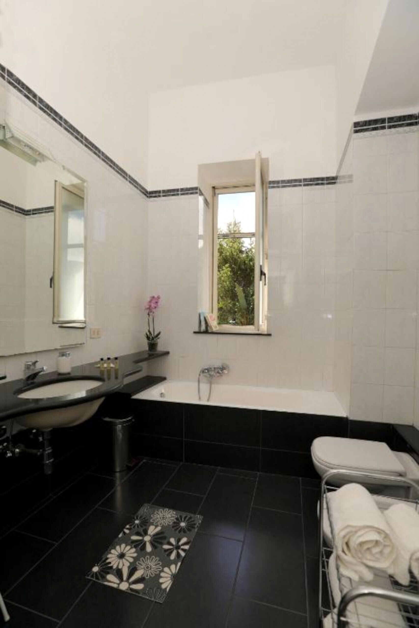 A modern bathroom with a large mirror, a bathtub, a window, and a towel rack.