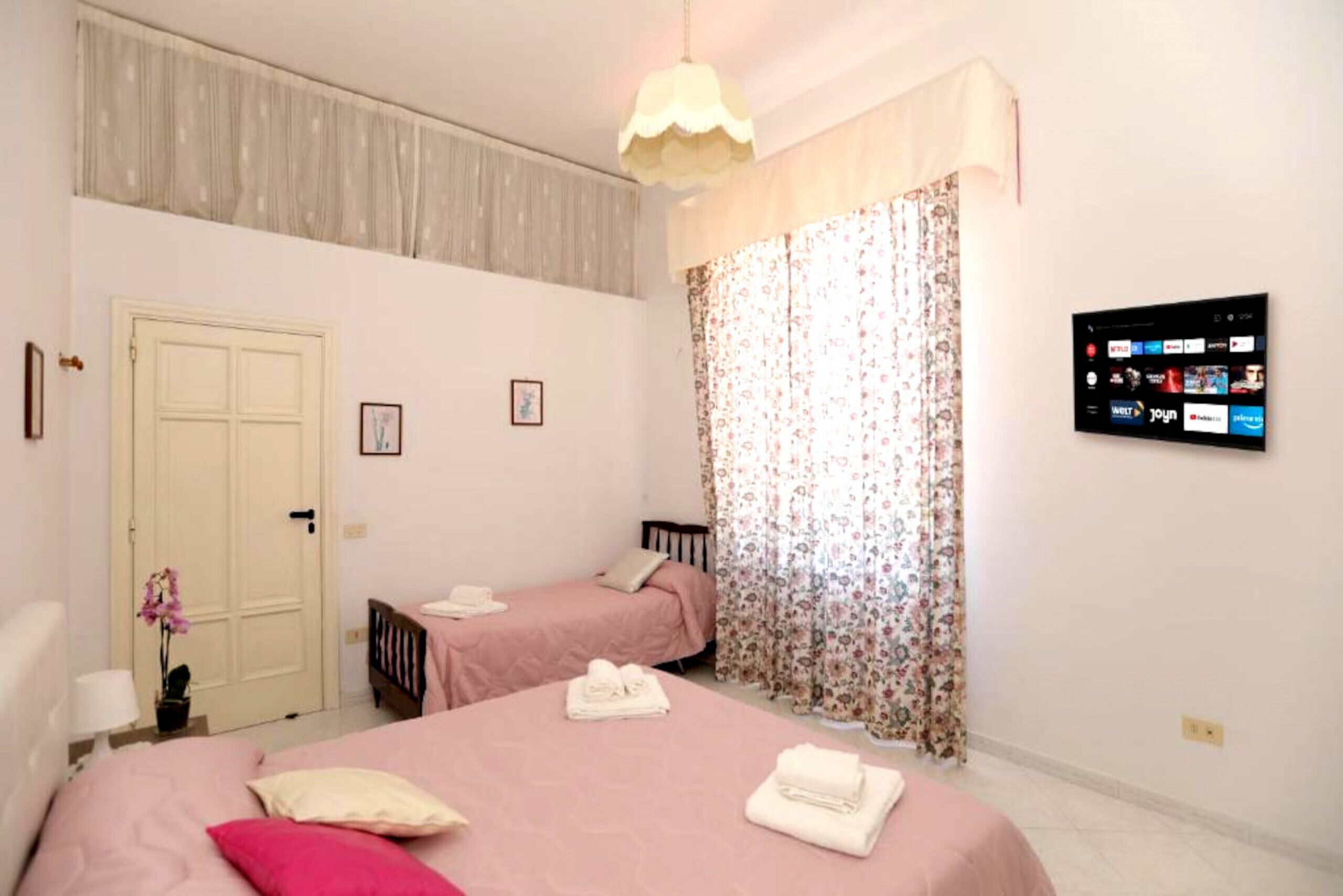 Habitación de hotel con dos camas, un televisor instalado en la pared y una puerta con cortina floral.