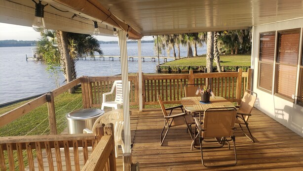 A wooden deck with outdoor seating, overlooking a lake with a dock and trees. - St. Johns River Retreat - CSC Unit 1 (Crescent City)