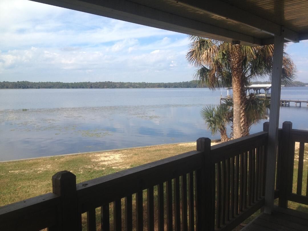 A view from a covered deck overlooking a lake with a distant shoreline and palm trees.